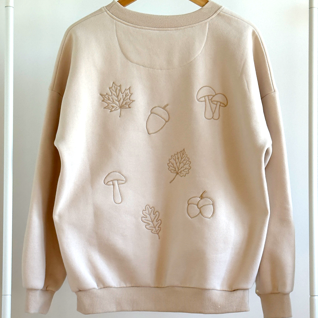 Beige sweatshirt with autumn-themed embroidery on a white background