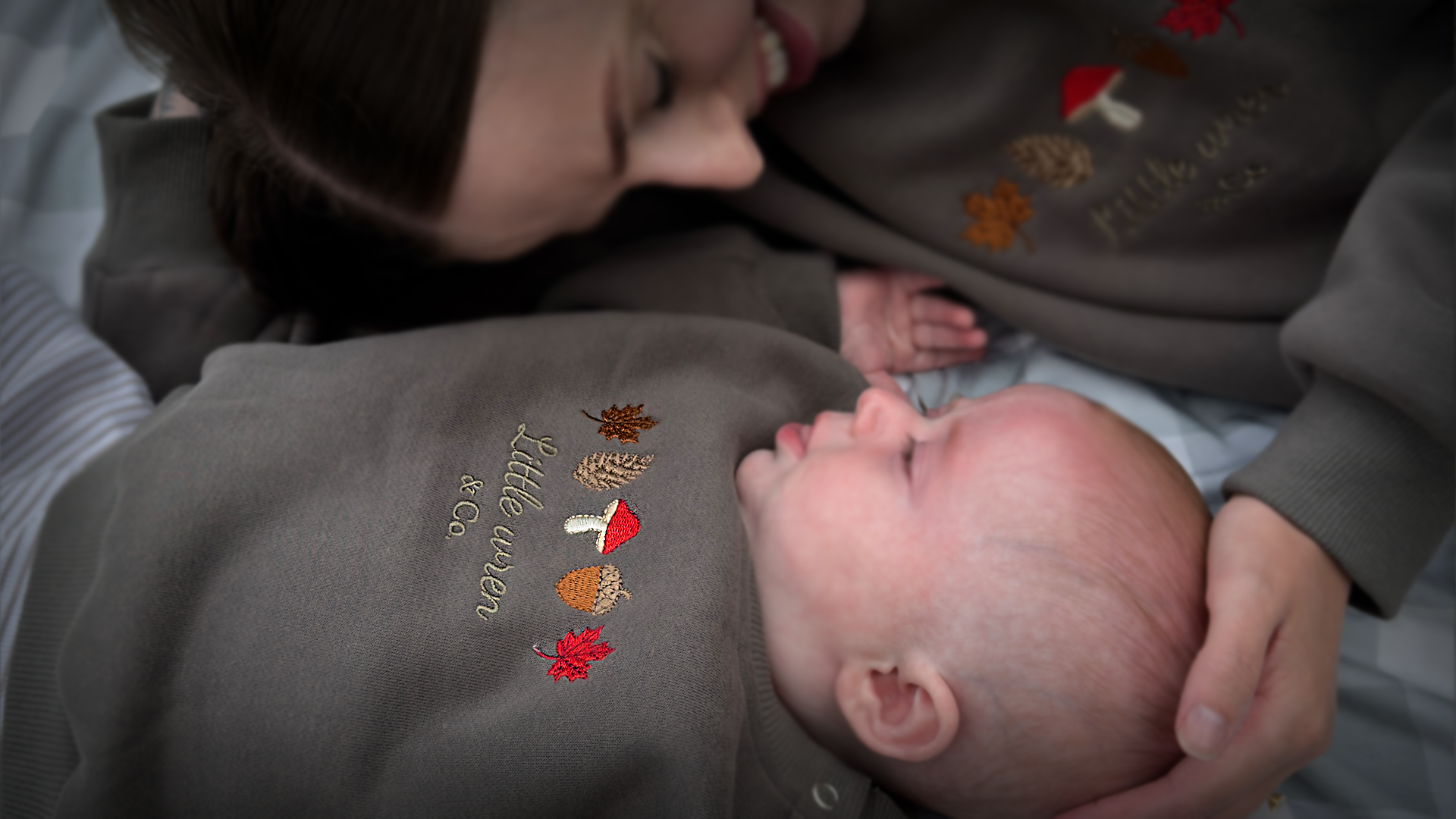 Person holding a baby wearing a hoodie with embroidered designs.