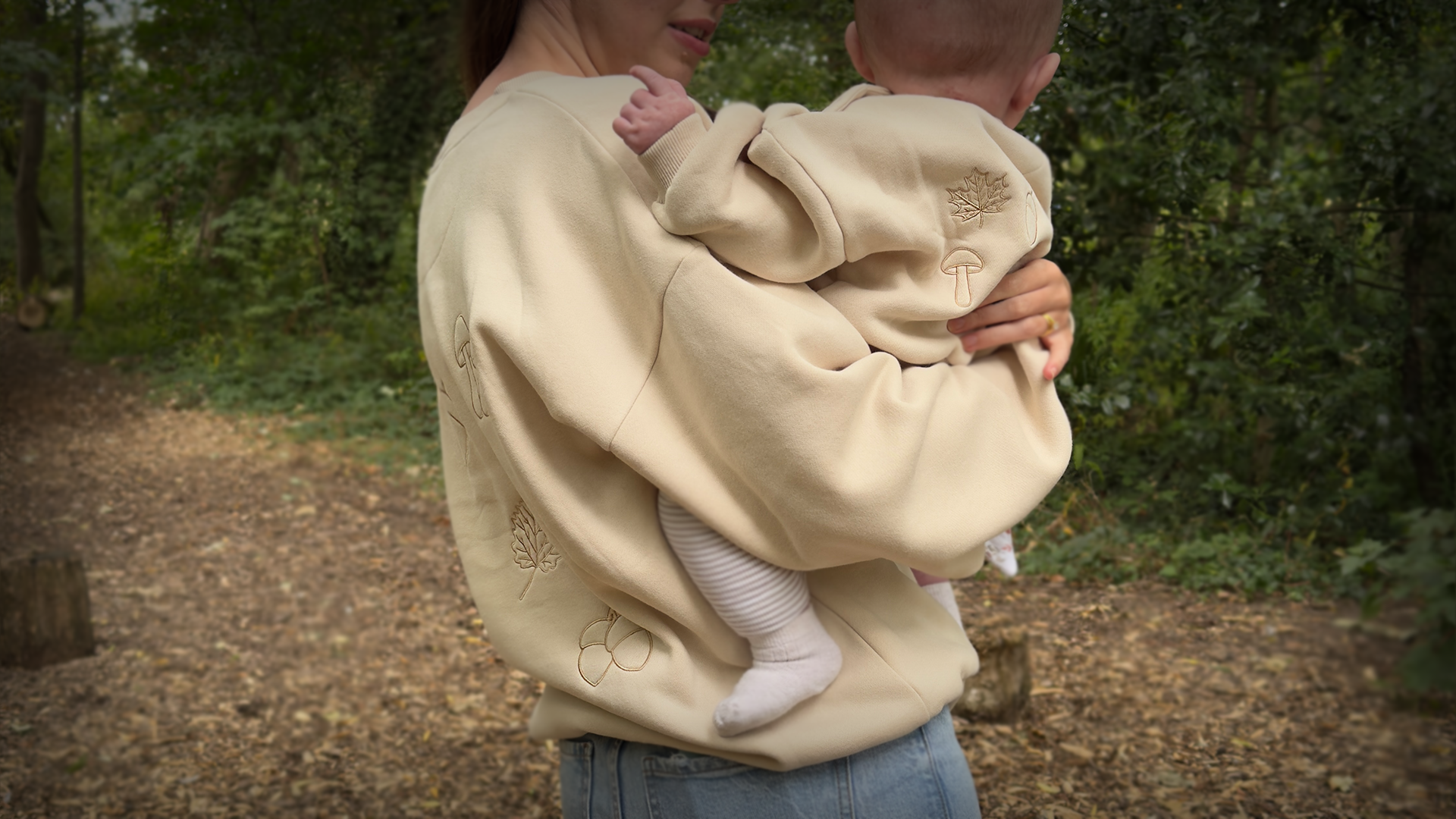 Person holding a baby in a beige carrier with a natural outdoor background